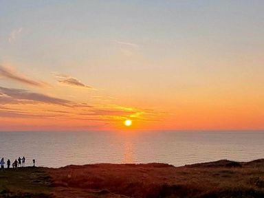 a sunset over the ocean with people silhouetted in the foreground at Perran Sands - Holiday Accommodation 8131 in Perranporth