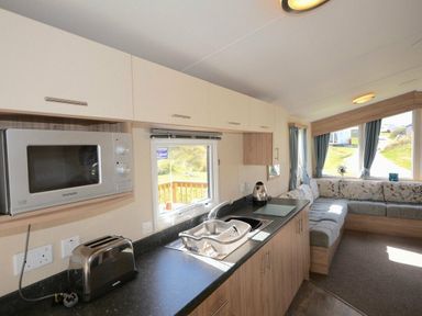 a kitchen area with a microwave, toaster, and sink next to a seating area at Perran Sands - Holiday Accommodation 8302 Perranporth