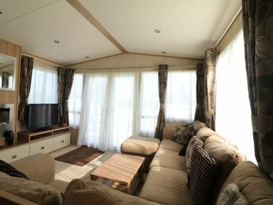 a living room with a sofa, television, and large windows with curtains at White Acres Holiday Park - Holiday Accommodation 895, Newquay