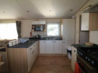 a kitchen area with a stove, refrigerator, and seating in White Acres Holiday Park - Holiday Accommodation 895, Newquay
