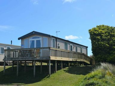 a mobile home with a wooden deck situated on grassy terrain at Perran Sands - Holiday Accommodation 8982 Perranporth