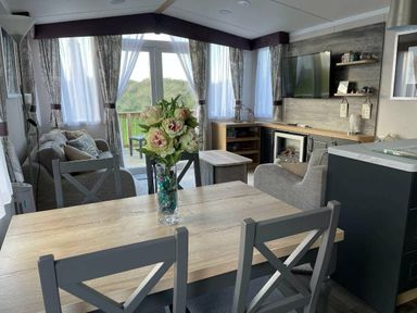 a living room with a dining table, large windows, and a TV unit at Perran Sands - Holiday Accommodation 8982, Perranporth