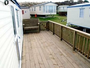 a wooden deck area with a bench and nearby caravans at Perran Sands - Holiday Accommodation 9159, Perranporth