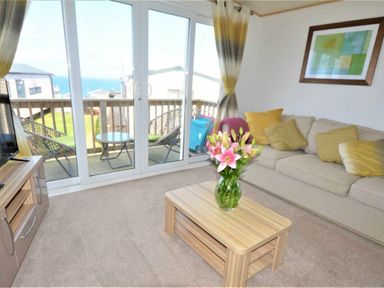 a living room with a sofa, coffee table, and large windows overlooking the sea at Perran Sands - Holiday Accommodation 9657 Perranporth