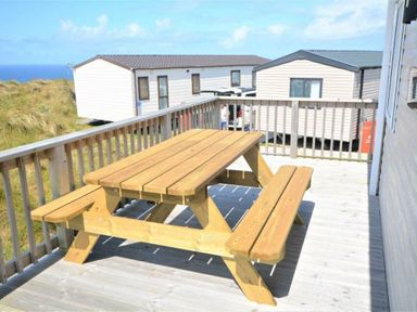 a wooden picnic table on a deck with caravans in the background at Perran Sands - Holiday Accommodation 9657 Perranporth