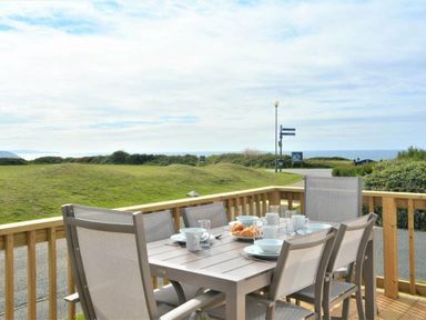 a dining area with a table set for breakfast overlooking a grassy area and the ocean at Perran Sands - Holiday Accommodation 9871 Perranporth