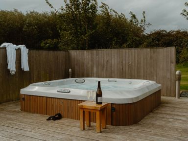 A hot tub with champagne and glasses on a wooden deck at Wellington in Wigton