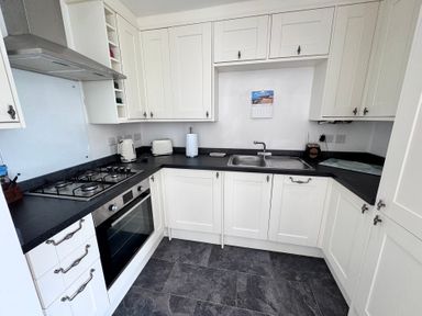 A kitchen with cabinets, stove, sink, and kettle at Ty Nain in Bodorgan