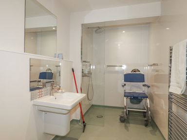 A bathroom with a sink, mirror, shower, and shower chair at Hillbre, Trevone