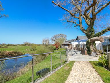 An outdoor area with a pathway, building, tree, and water at Glamping Pod 1, Oldwalls, Llanrhidian, Gower