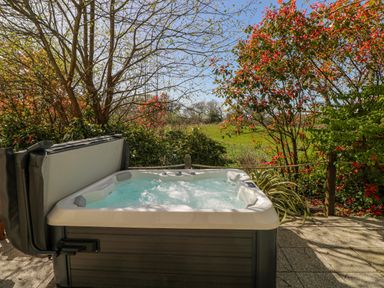 A hot tub in a garden with plants at Oak Tree Cottage Oldwalls, Llanrhidian, Gower