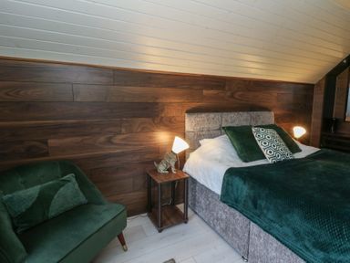 A bedroom with a bed and armchair at Garden lodge 3 in Swansea