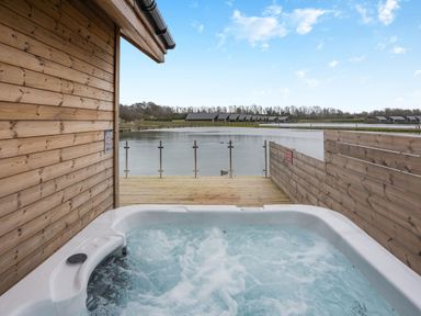 A hot tub on wooden decking overlooking water at Tranquillity 3 in Warton near Carnforth