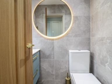 A bathroom featuring a toilet, sink, mirror, and wooden door at Pistyll Ddu in Brynsiencyn near Llanfairpwllgwyngyll