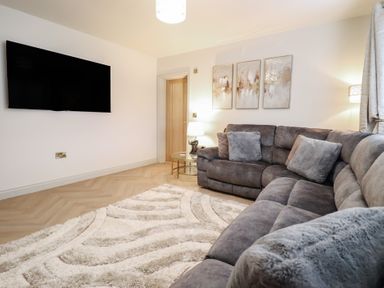 A living room with a gray sofa and television at Pistyll Ddu in Brynsiencyn near Llanfairpwllgwyngyll