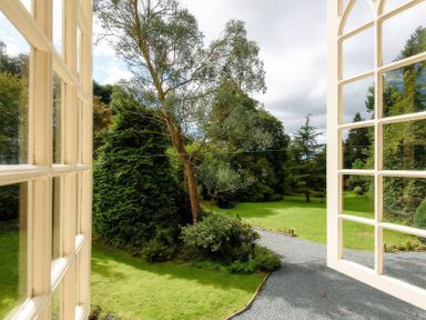 A view of a garden with trees and a pathway from a window at Ladye Park in Liskeard