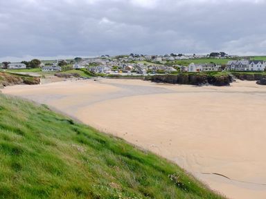 A beach with sand and grass along with distant houses at Hillbre Shepherd Hut Padstow