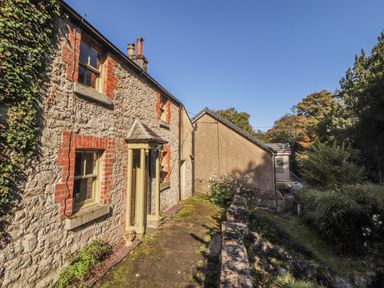 An exterior view of a stone cottage with a porch and a shed at Rock Cottage in Milnthorpe