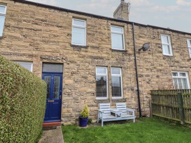 A stone exterior with a blue door and windows at 23 Northumbria Terrace Amble