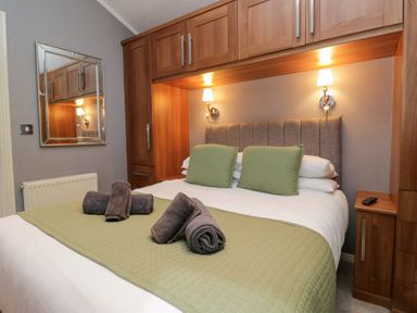A bedroom with a double bed and wooden storage at 32 Grasmere, White Cross Bay near Windermere