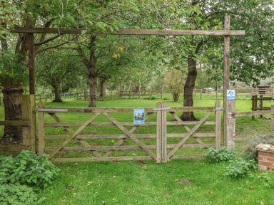 A gate leading to a grassy area with trees at Duchess Cottage in Woodbridge