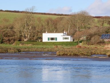 A house next to water with trees and solar panels at Bryncyn Newport, Pembrokeshire