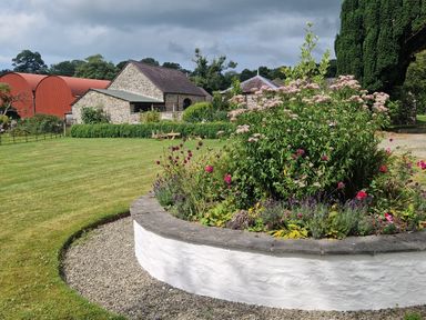 A garden with flowers and a stone wall at Secret Garden Cottage in Ciliau Aeron near Aberaeron