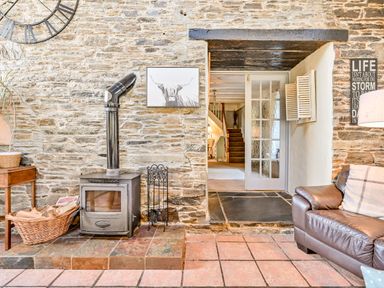 A living room with a stove and wooden table at The Old Farm House near Pelynt