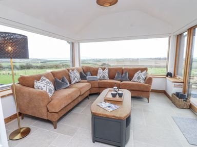 A conservatory with a brown sofa and a coffee table at 2 Trem Y Mor Llanfwrog near Llanfachraeth