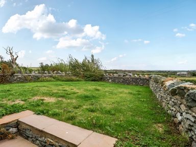 A garden with a stone wall and grass at 2 Trem Y Mor Llanfwrog near Llanfachraeth