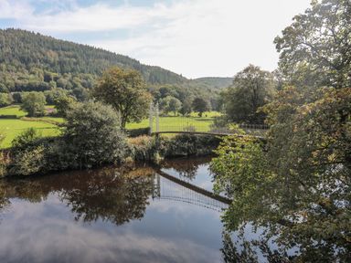 A river with a suspension bridge and surrounding trees at Green Bank Betws-Y-Coed