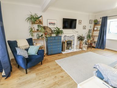 A living room with a television and blue armchair at 16 Ffordd Meigan in Beaumaris