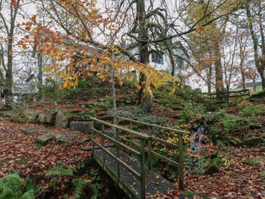 A view of a house with a bridge and trees at Chapel Hill in Catlowdy