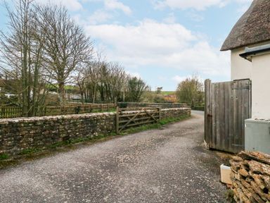 A gravel road with a stone wall and trees at Long Barn in Burton Bradstock