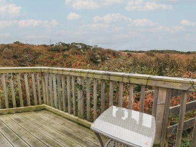 A wooden outdoor patio with a table and chair overlooking a natural landscape at Peaceful in Stranraer