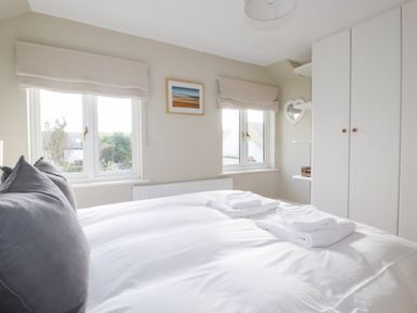 A bedroom with a bed, towels on the bed, and windows at The Mizzen in St Endellion near Port Isaac