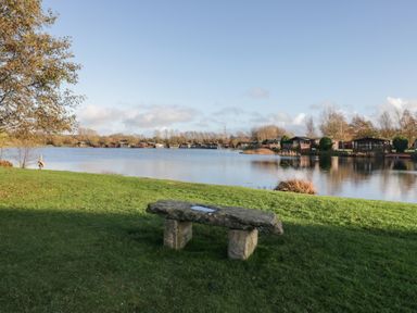 A lake with a stone bench and trees at Bluebell Lodge in Warton