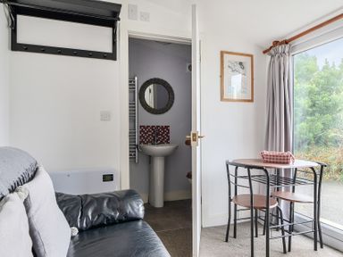 A living room with a dining table and a sink in the background at The Nook in Praa Sands