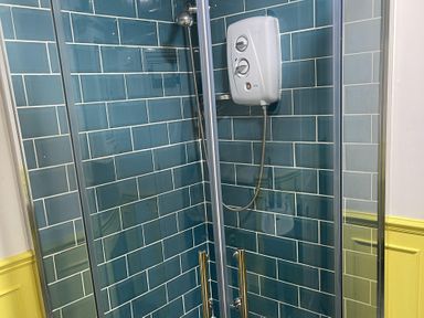 A shower with glass doors and blue tiled walls at High Dyke Cottage