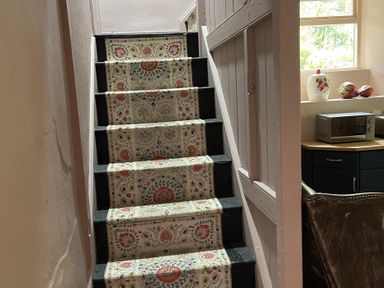 A staircase with patterned carpet leading to a window and kitchen area at High Dyke Cottage