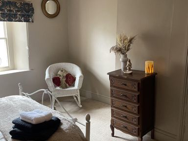 A bedroom with a bed, dresser, chair, and decorative flowers at High Dyke Cottage