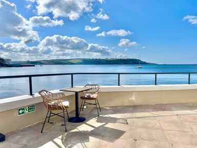 An outdoor seating area with two chairs and a table overlooking the water at Seafront Cottage