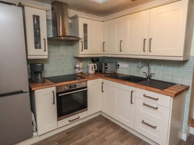 A kitchen featuring a refrigerator, oven, sink, coffee maker, and cabinets at Corner Cottage in Seahouses