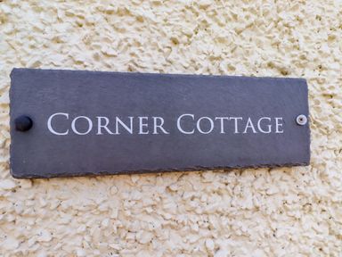 A slate sign displaying 'Corner Cottage' on an outdoor wall