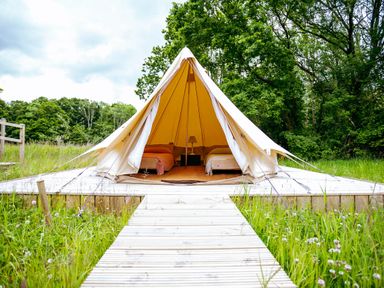 A tent with beds inside on a wooden deck in a field
