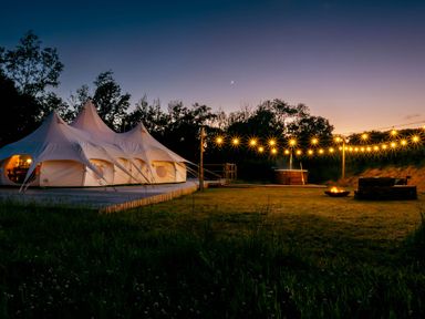 A tent with string lights and a fire pit at an outdoor space