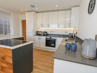 A kitchen with cabinets, a microwave, kettle, and mugs at Sea Fern House - 36 Poole