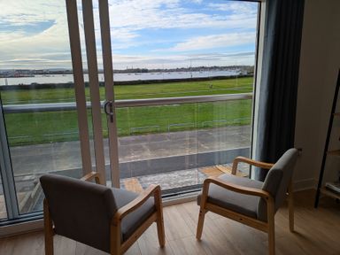 A living room with two chairs and a view of grass and water at Sea Fern House - 36 Poole