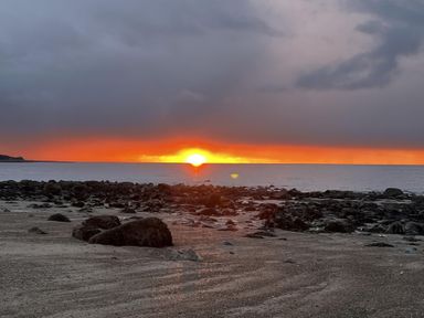 A sunset over the ocean with rocks and sand at Bwthyn Nain 