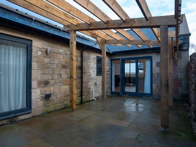 An outdoor patio with a pergola and stone walls at The Shearling in Morpeth